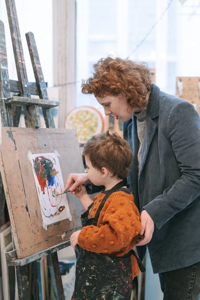 A young child learning to paint with guidance from an instructor in a vibrant art studio.